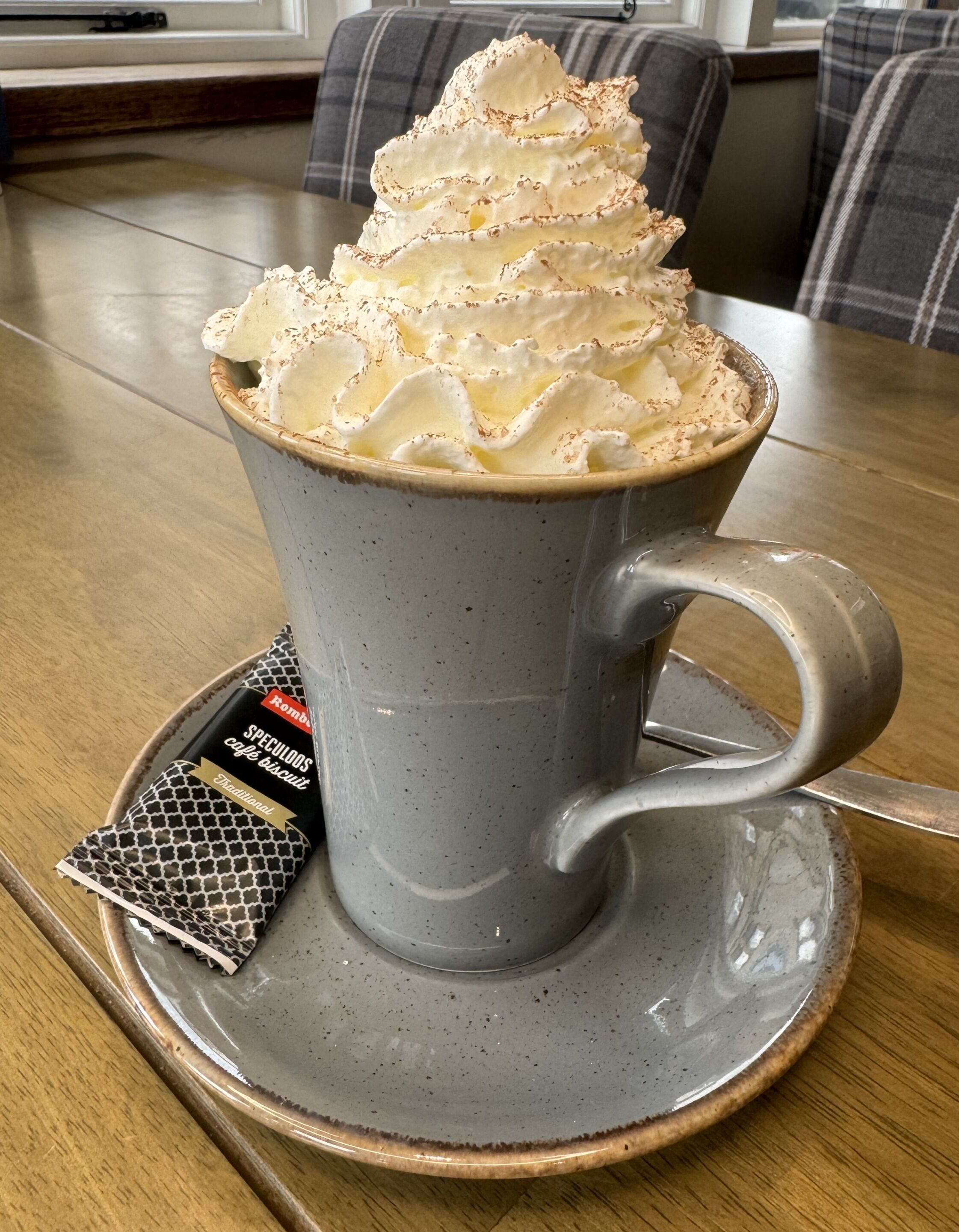 Una tassa de cafè amb nata muntada i un paquet de galetes speculoos sobre un plat.