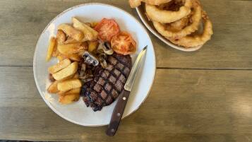A plate with steak, fries, mushrooms, and tomatoes, and a separate plate with onion rings.