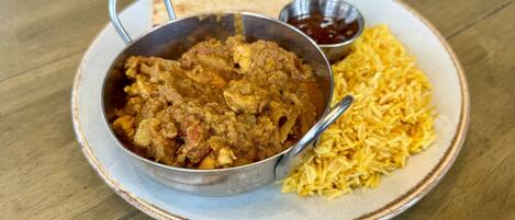 Ein Teller mit einem Currygericht und Reis, dazu ein Fladenbrot und eine kleine Schale Soße.