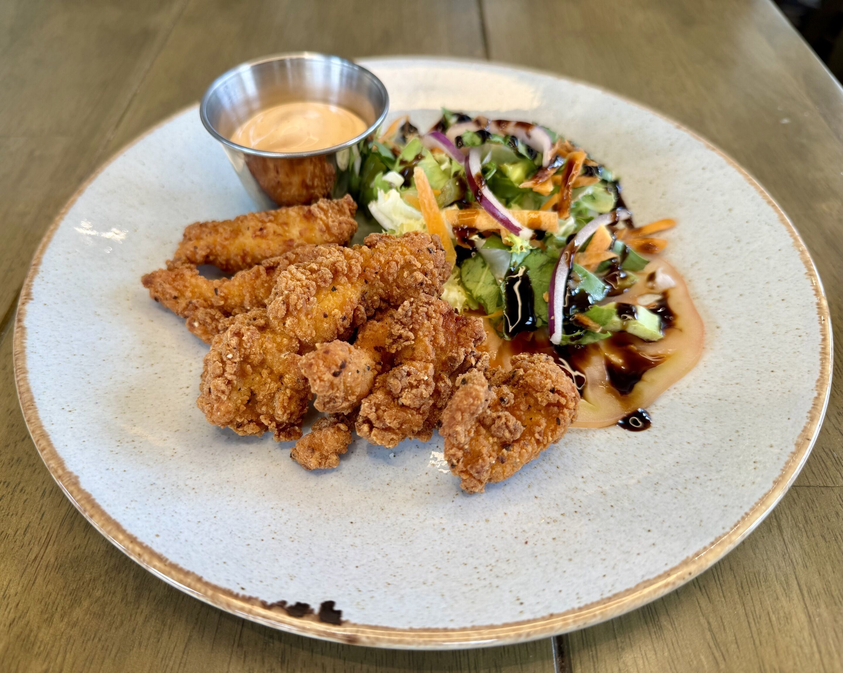 Un plato con pollo frito, una ensalada y una salsa acompañante.