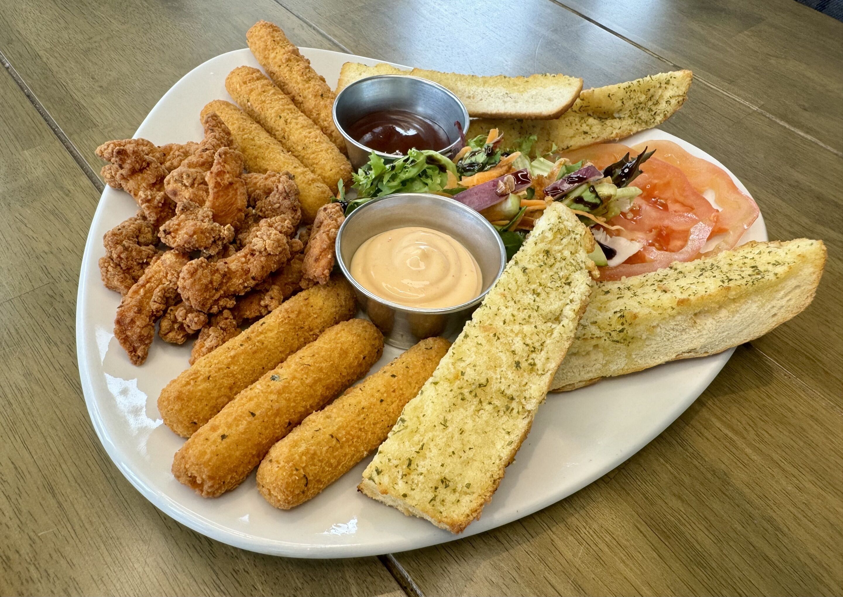 Une assiette de nourriture comprenant du poulet frit, des bâtonnets de mozzarella, une salade et du pain.