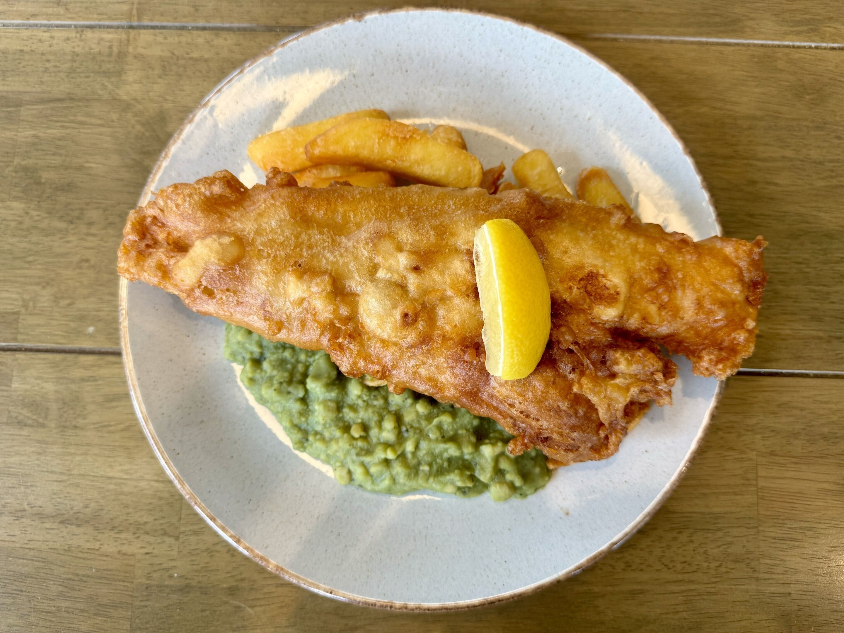 A plate with a fish fillet, chips, and mashed potatoes.