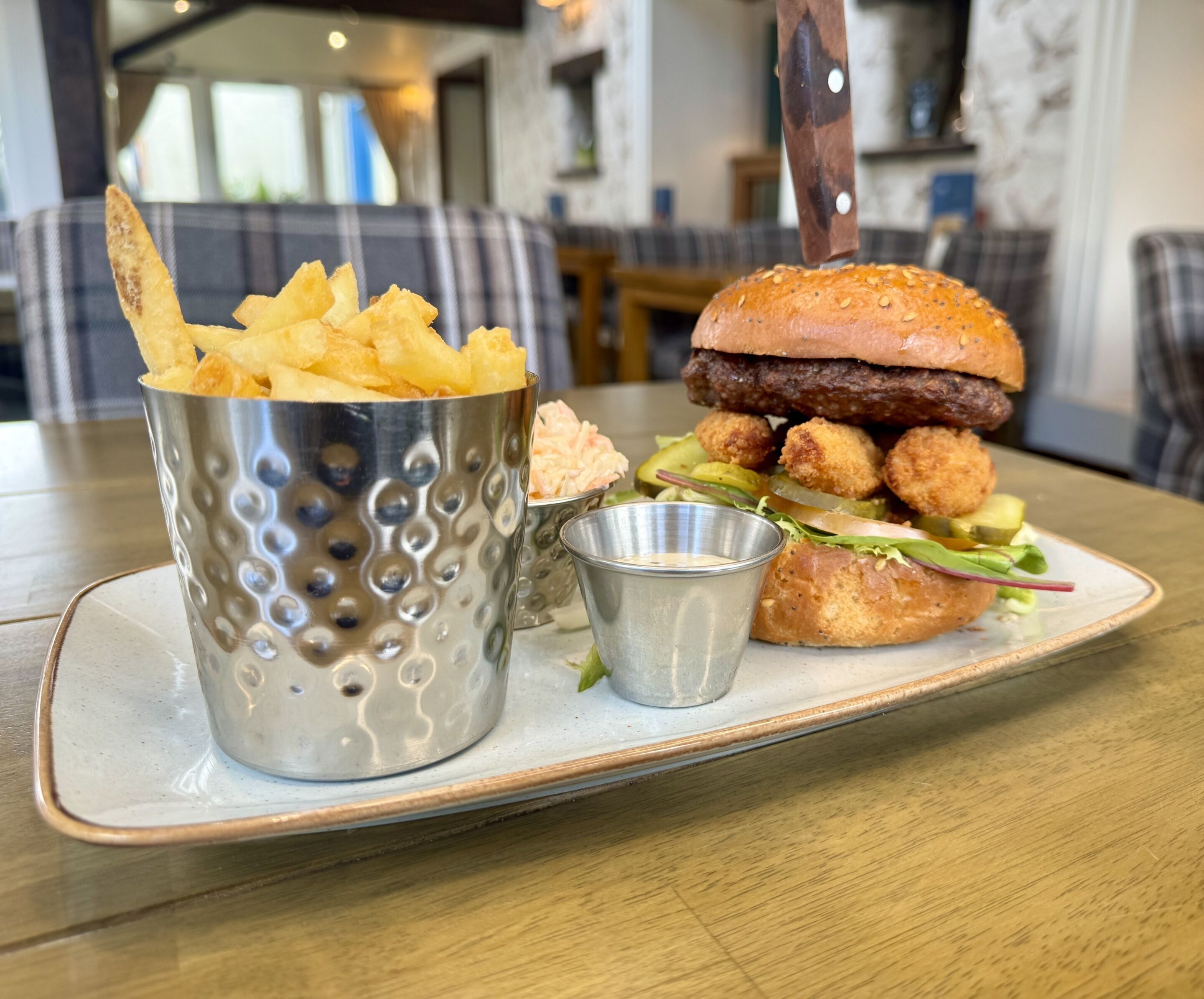 A meal consisting of a burger with a sesame seed bun, a side of tater tots, and a cup of chips on a ceramic plate.