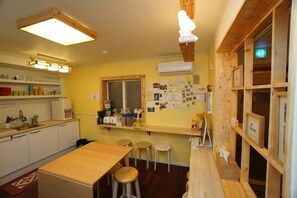 A compact kitchen with a wooden table and stools, a window with notes, and a wall-mounted air conditioner. - 710 Guest house Yellow (Busan)