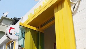 Entrada a un hostal con una puerta amarilla y verde, una antena parabólica y un ventanal pequeño.
