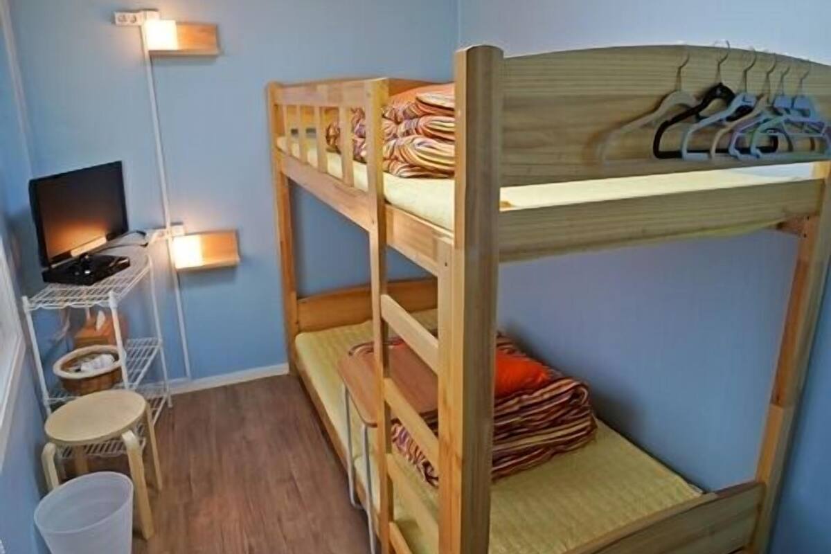 A bunk bed room with a desk and chair, a television, and a hanging rack.