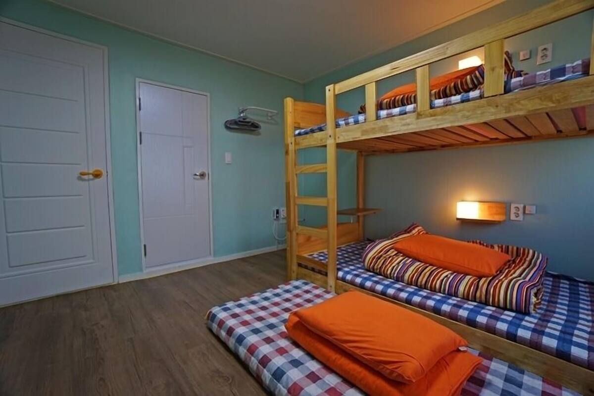 A bunk bed room with a checkered mattress, a wooden ladder, and a wall-mounted light fixture.