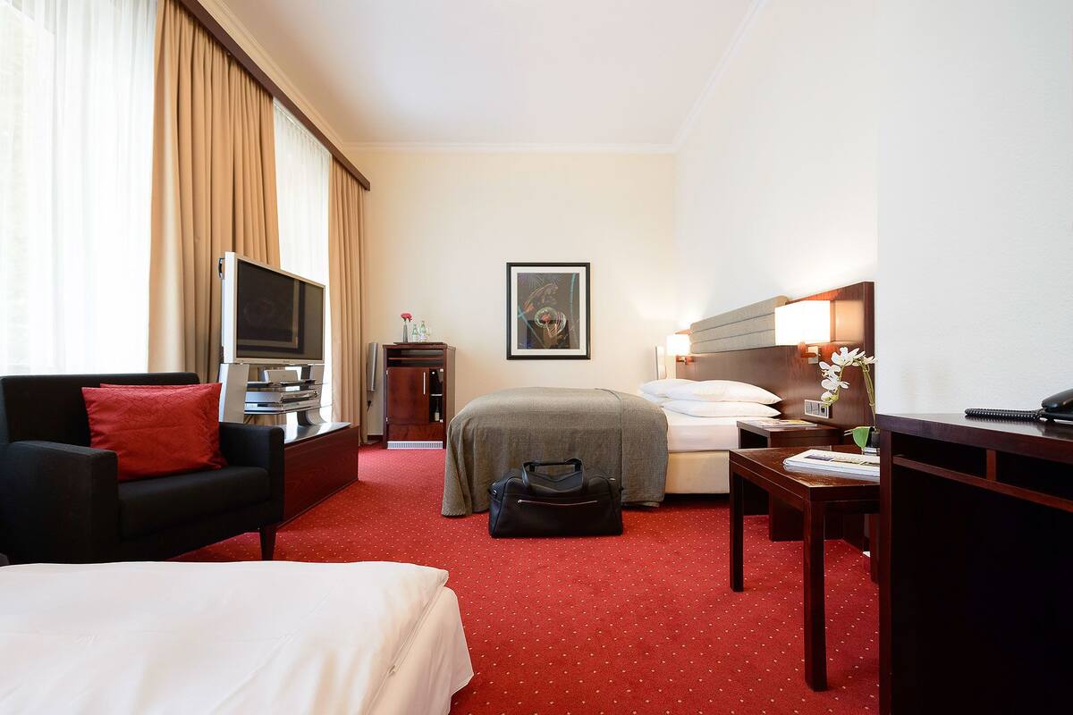 A hotel room with a bed, a desk with a computer, a TV, and a chair.