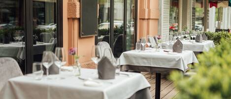 A restaurant with outdoor seating, white tablecloths, and neatly arranged dining tables.