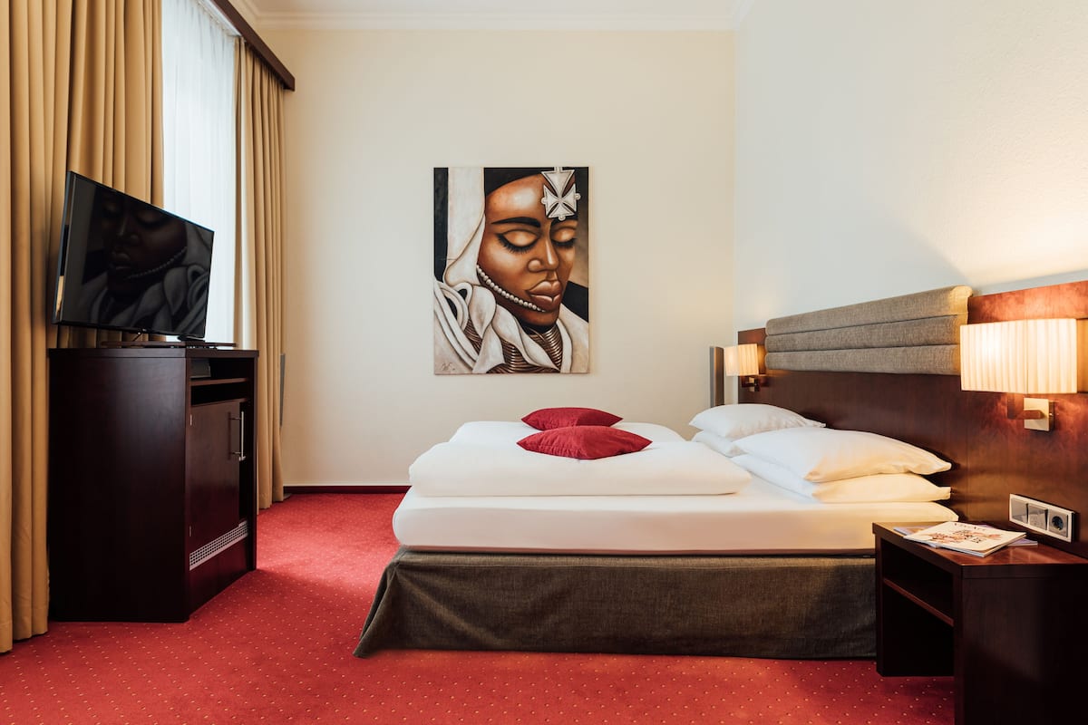A hotel room with a bed, a TV, a painting, and a nightstand.