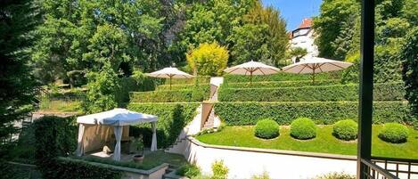 A landscaped garden with a gazebo, neatly trimmed hedges, and a staircase leading to a building.