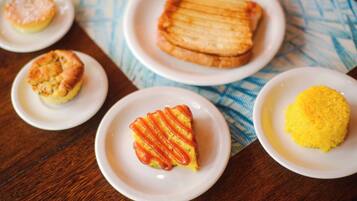 Uma mesa com diversos alimentos em pratos brancos, incluindo uma fatia de bolo com listras vermelhas, um muffin e uma sobremesa amarela.