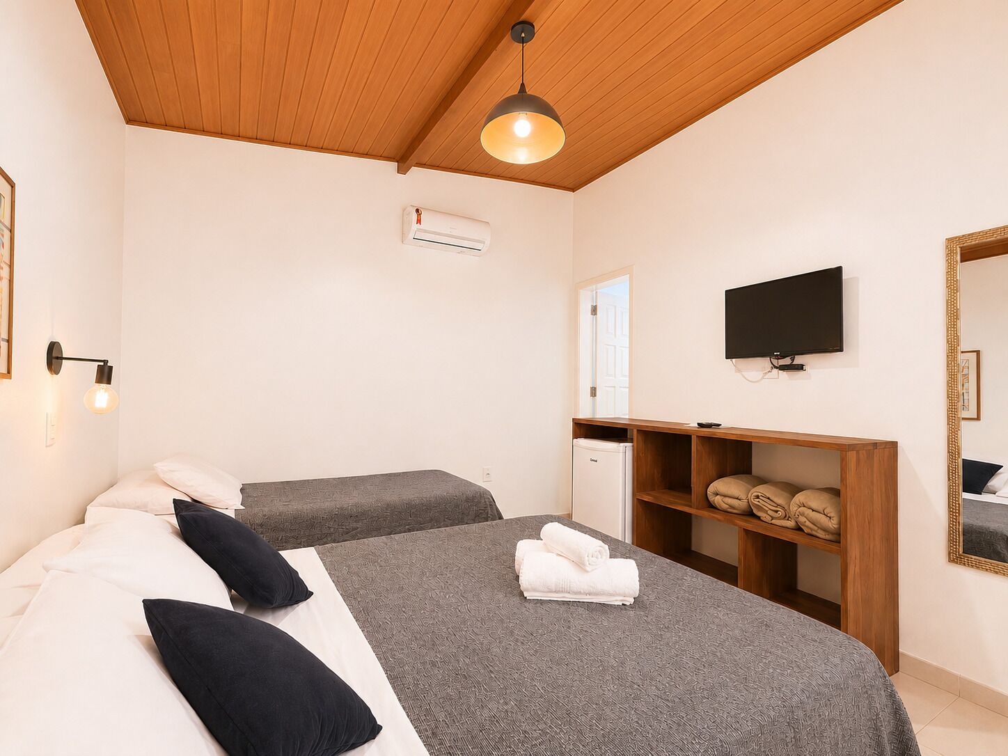 Een slaapkamer met twee bedden, een houten plafond, een televisie, een spiegel en een kleine kitchenette.