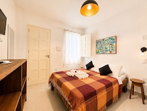 Ein Schlafzimmer mit Bett, Schreibtisch, Stuhl, einem Gemälde und einer Tür.