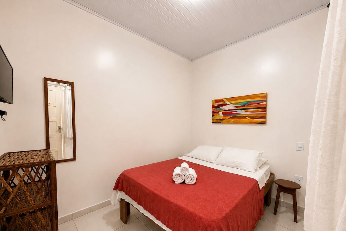 A bedroom with a bed, a mirror, a painting, and a small stool.