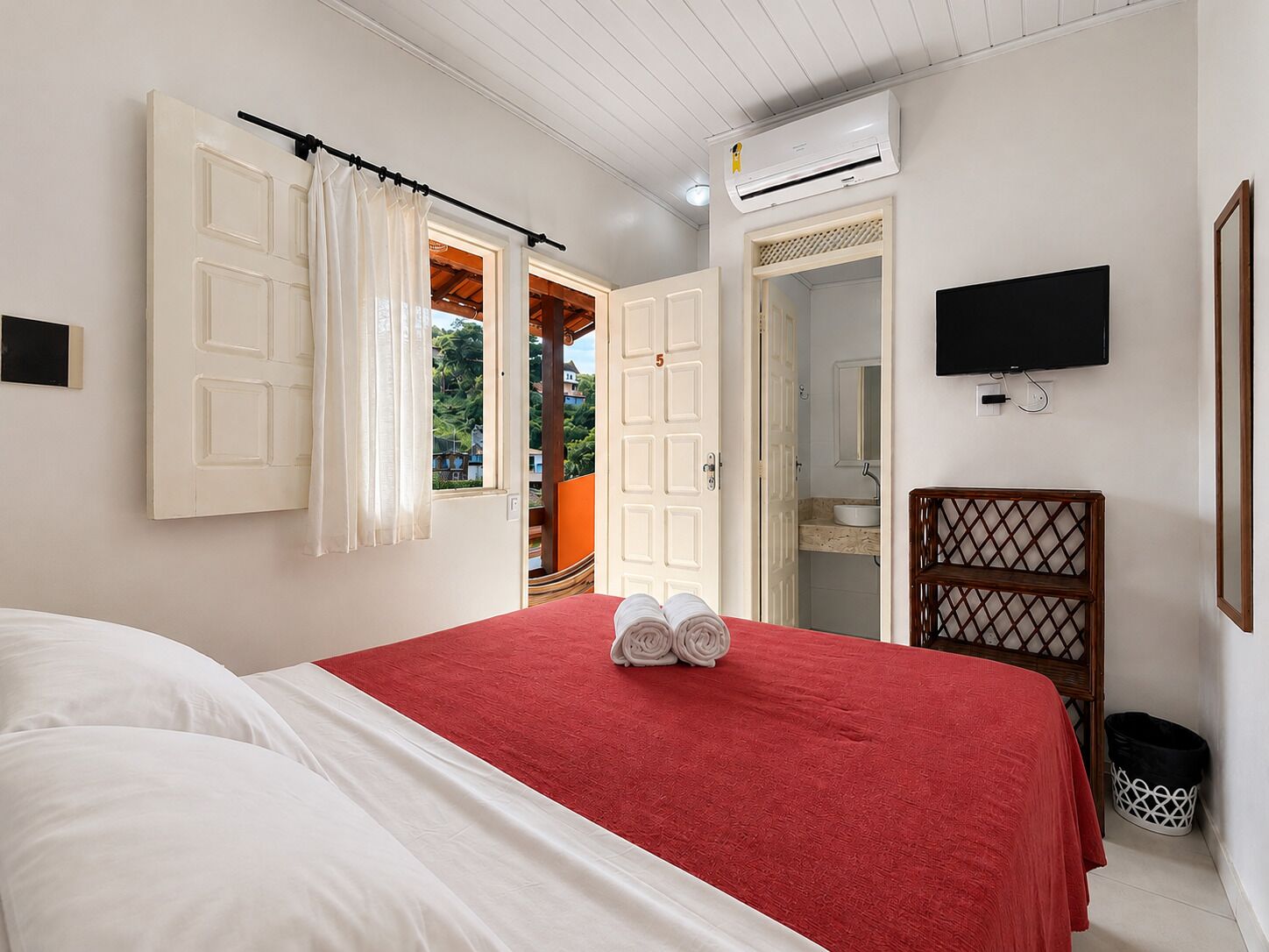 A bedroom with a bed, a TV, an air conditioning unit, and a view of the outside.