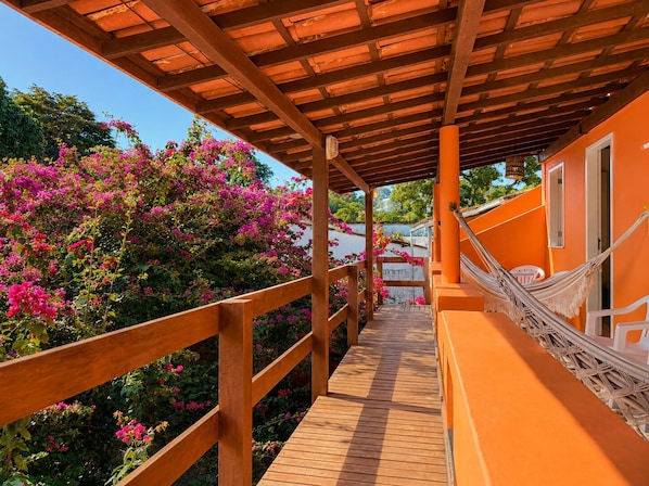 A wooden deck with a railing, leading to an orange building with a window and a door. - Pousada Aconchego (Cairu)