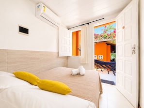 A hotel room with a bed, a window, an air conditioning unit, and an open door leading to an outdoor area. - Pousada Aconchego (Cairu)