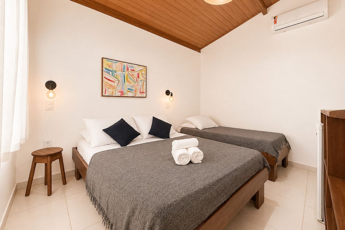 A bedroom with two beds, a ceiling fan, a painting, and a small bedside table.