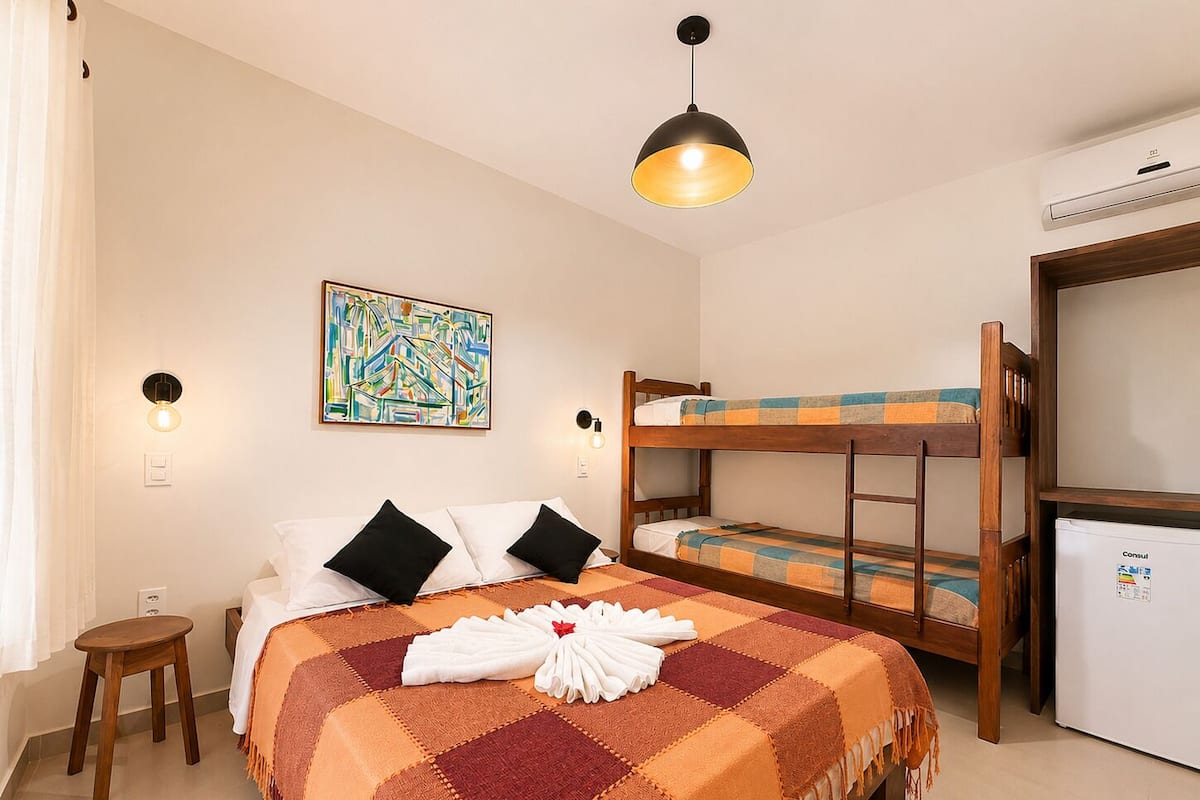 A room with a bed, a bunk bed, a small table, a wall-mounted light, a painting, and a ceiling light fixture.