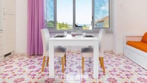 A dining area with a table and chairs, a window with a view, and a sofa. - Artis Domus Relais & Spa (Sorrento)
