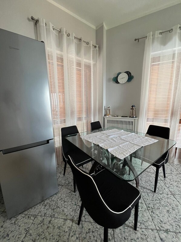 Una cocina compacta con una mesa de comedor de vidrio, cuatro sillas, un refrigerador y un radiador.