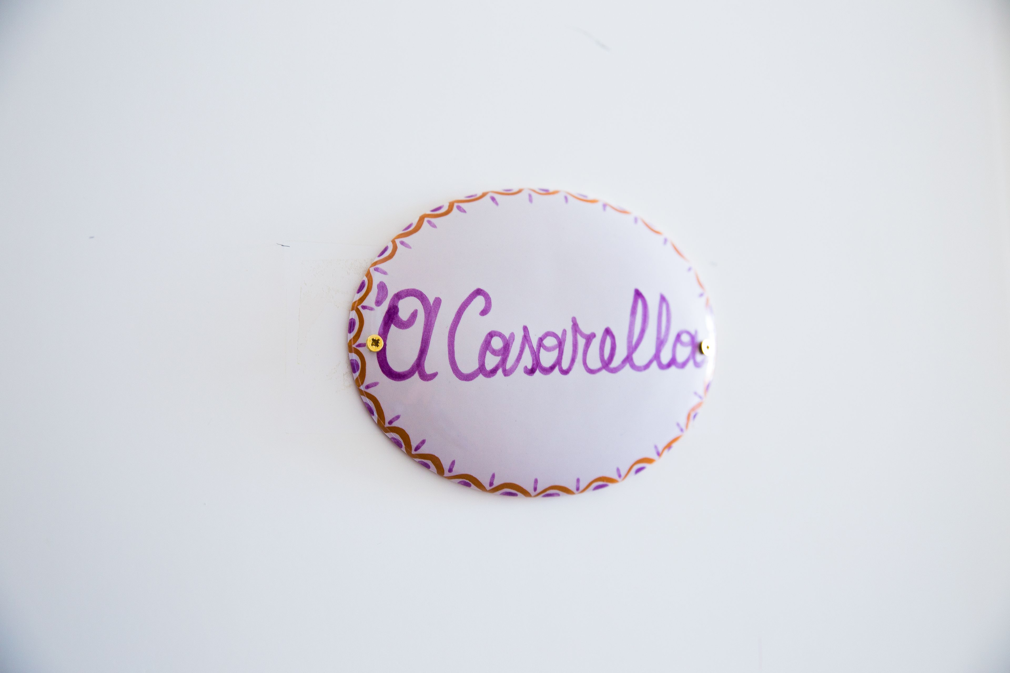 Un panneau rond et blanc portant l’inscription « El Casarello » en violet.