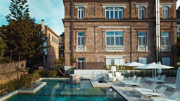 A pool area with lounge chairs and umbrellas, surrounded by a brick building with large windows and a stone wall. - Artis Domus Relais & Spa (Sorrento)