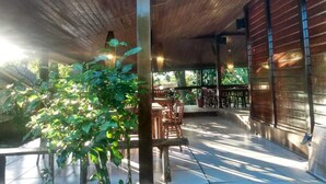 An outdoor patio area with wooden tables and chairs, surrounded by greenery and a wooden ceiling structure. - Pousada Paraiso de Boipeba (Cairu)