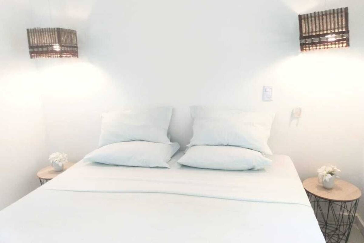 A bed with white bedding, two bedside tables with small vases, and wall-mounted light fixtures.