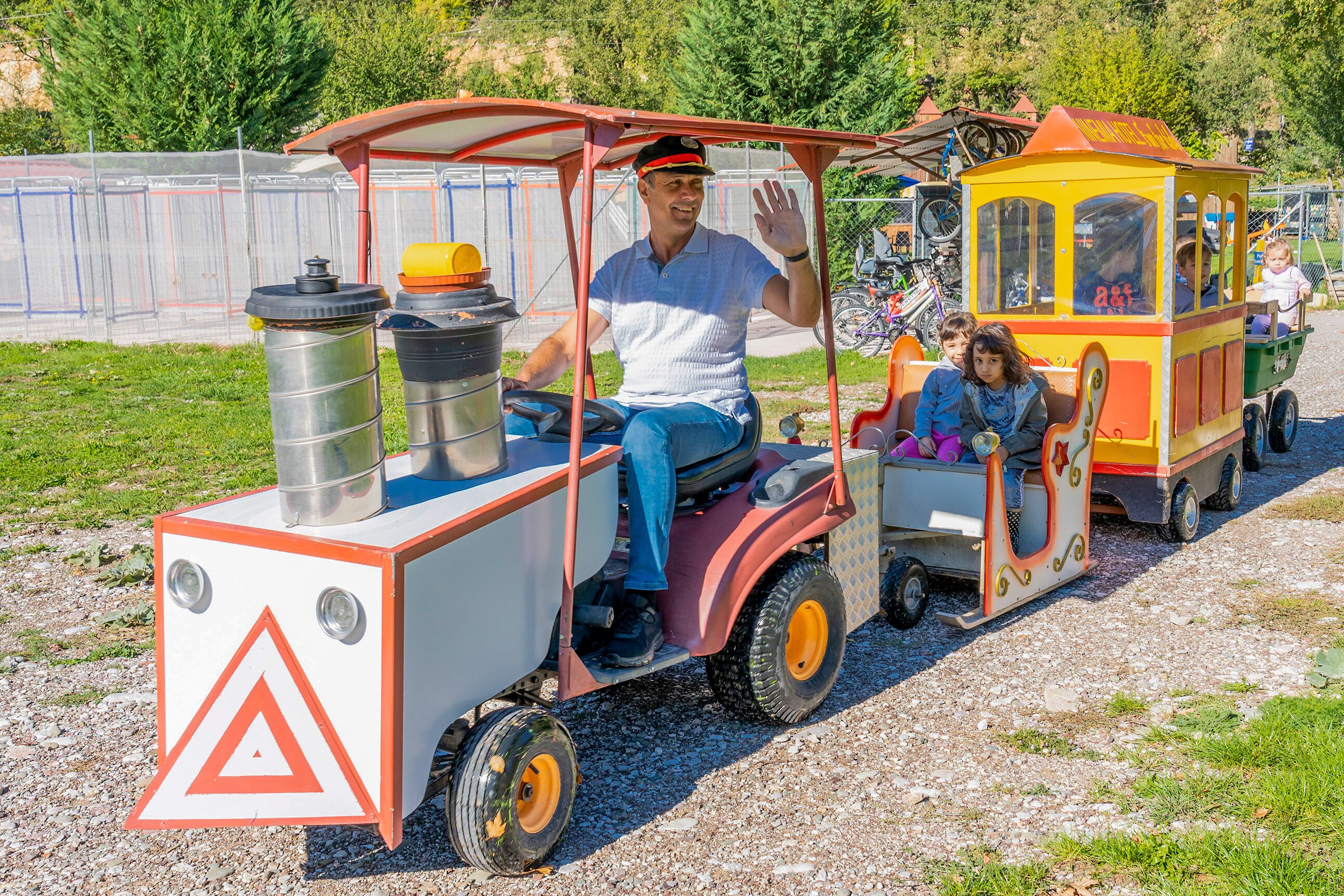 A small, colorful train with passengers, including children, traveling on a gravel path.