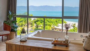 A room with a large window, a wooden table, a white bathtub, and a wicker chair. - Pousada dos Sonhos (Florianópolis)