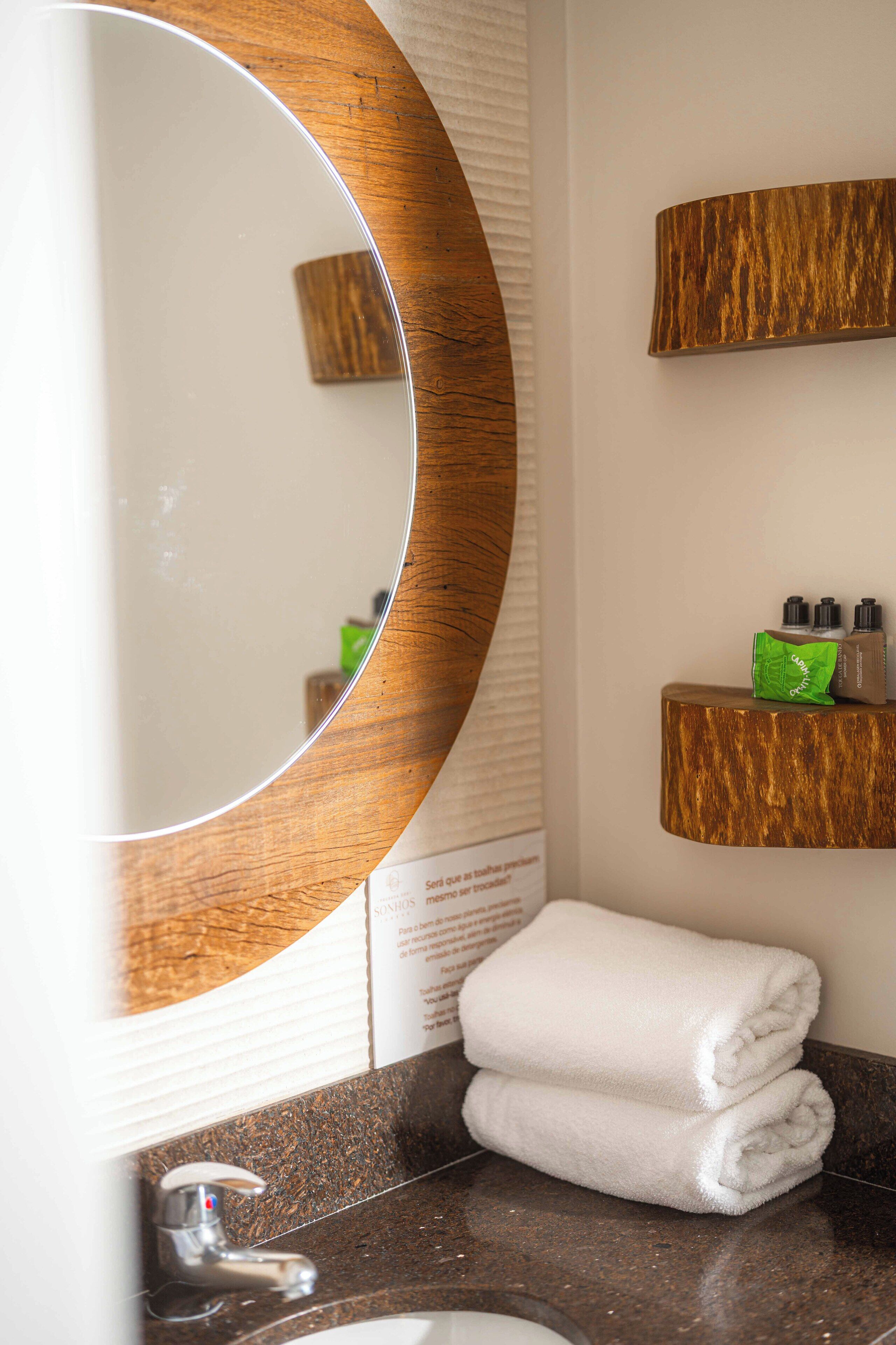 Un ba ño con un espejo redondo, un lavabo, una toalla y un estante con artículos de aseo.