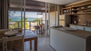 A modern kitchen with a large island, wooden shelves, and a view of the ocean. - Pousada dos Sonhos (Florianópolis)