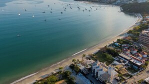 An aerial view of a coastal town with a beach, boats, and buildings. - Pousada dos Sonhos (Florianópolis)