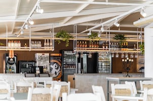 Uma área de bar com prateleiras de garrafas de bebidas, um minibar e plantas penduradas.