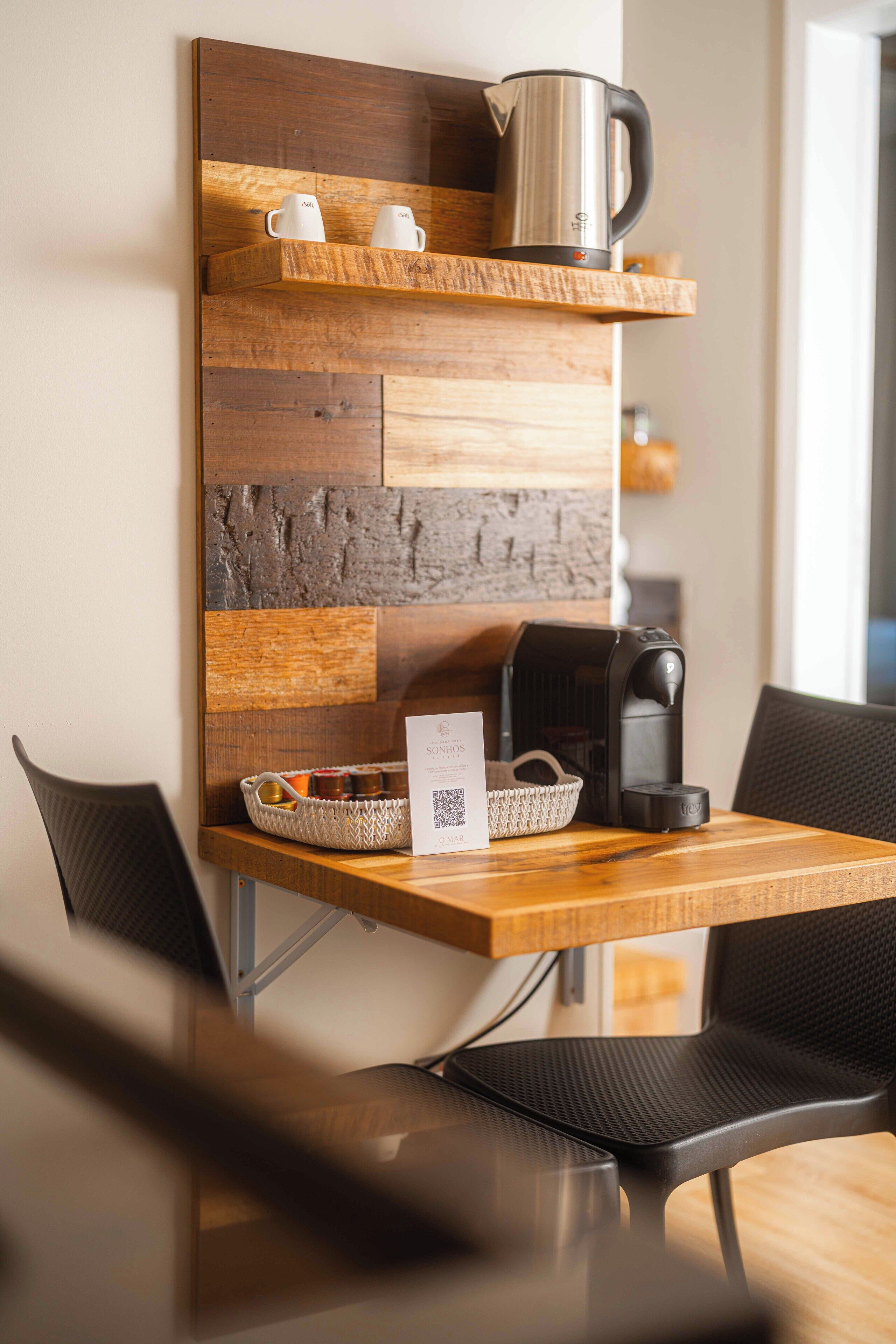 A modern coffee station with a wooden wall-mounted shelf, a coffee maker, and a basket of pastries.