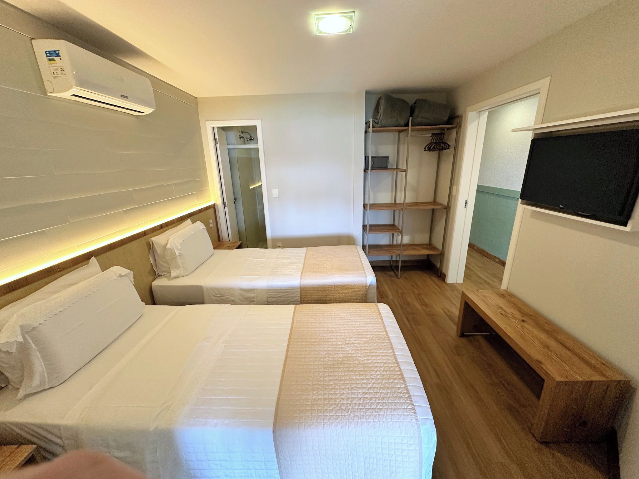 Habitación de hotel con dos camas, ducha, televisor y un banco de madera.
