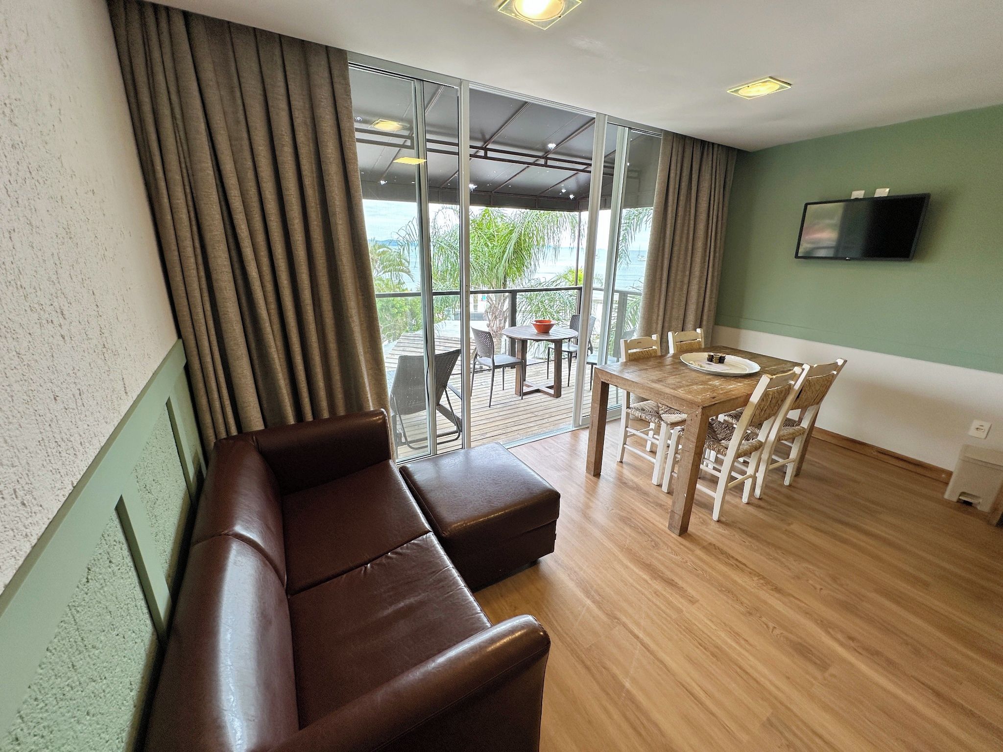 Une pièce moderne avec un plancher en bois, un canapé en cuir marron, une table à manger avec des chaises et un téléviseur fixé au mur.