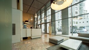Un moderno vestíbulo de hotel con una recepción, zona de estar y grandes ventanales con vistas a la ciudad.