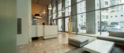 A modern hotel lobby with a reception desk, seating area, and large windows offering city views.