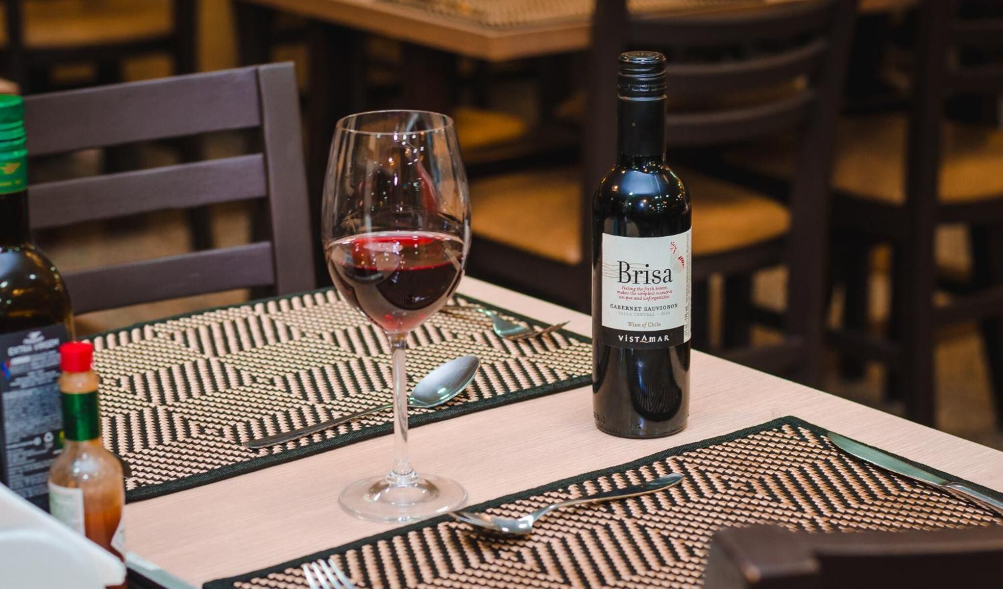 A table with a bottle of Brisa wine, a glass of red wine, and a spoon.