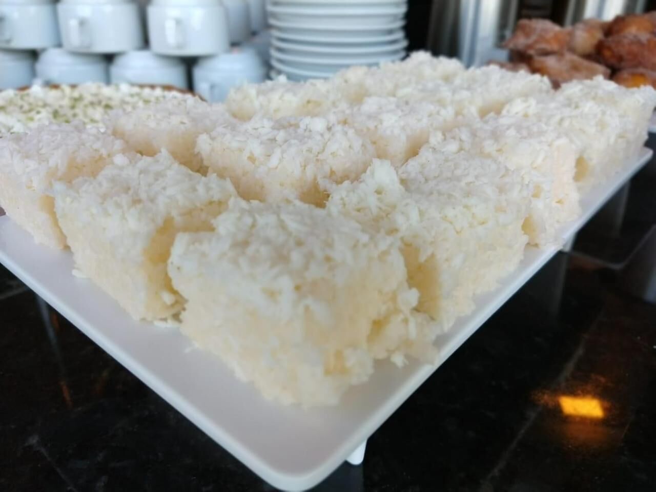 A white plate with a food item, possibly rice, on a dark surface.