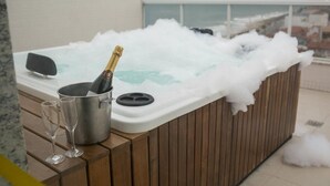 Boblebad med champagneflaske og to glas på en træterrasse med havudsigt.