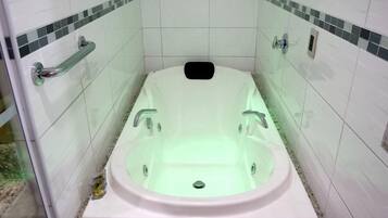 A bathroom with a white bathtub, chrome fixtures, and tiled walls with a green and white pattern.