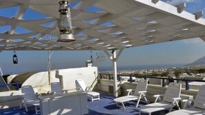 Una terraza en la azotea con sillones blancos y una mesa, con vistas a la ciudad y una montaña distante.