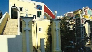 Un edificio amarillo con una escalera que lleva a una puerta, una ventana pequeña y un contenedor de basura.