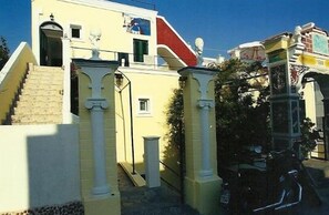 Un edificio amarillo con una escalera que lleva a una puerta, una ventana pequeña y un contenedor de basura.