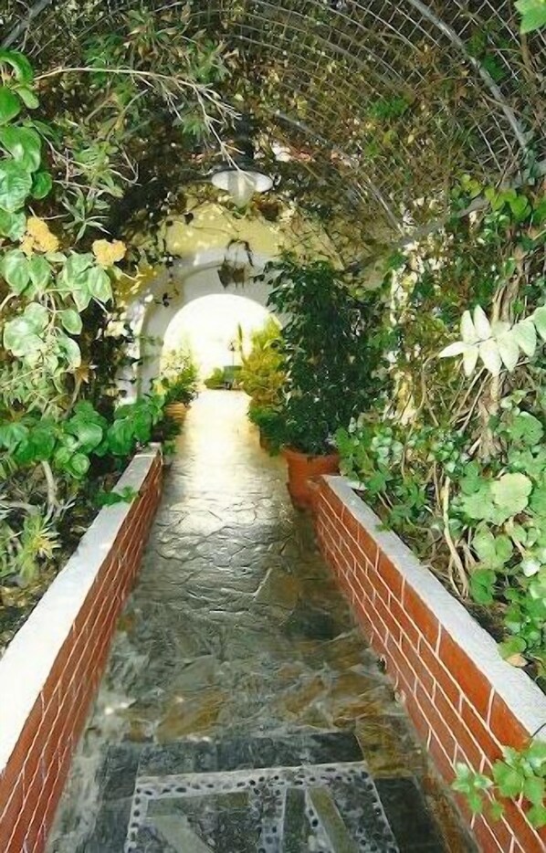 Un sendero de piedra que atraviesa un túnel exuberante y verde, con paredes de ladrillo y un arco de metal.