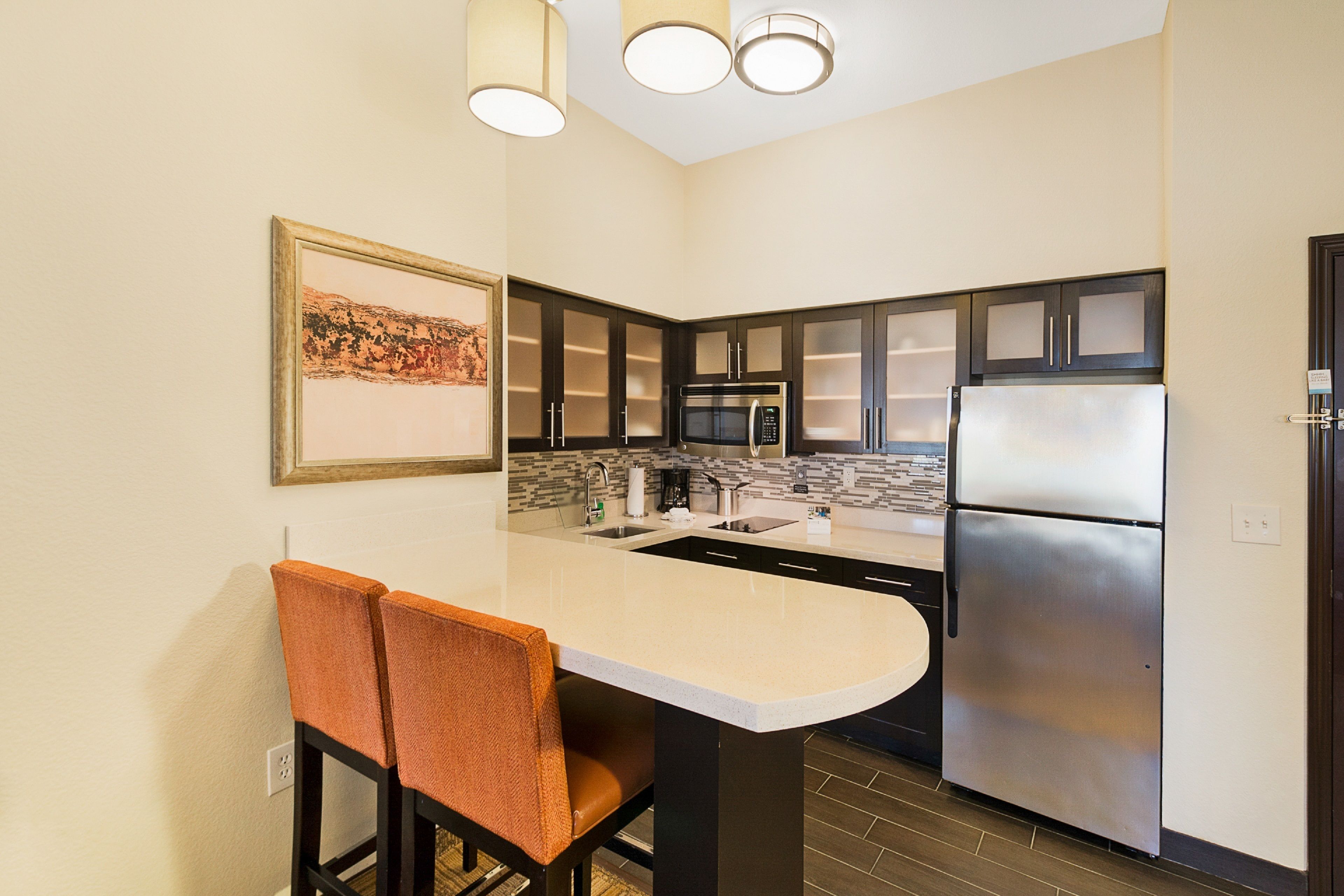 A modern kitchen with dark cabinets, a stainless steel refrigerator, and a white countertop.